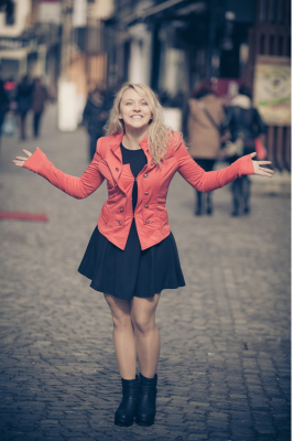 mulher loira feliz na sorrindo na rua com os braços abertos.